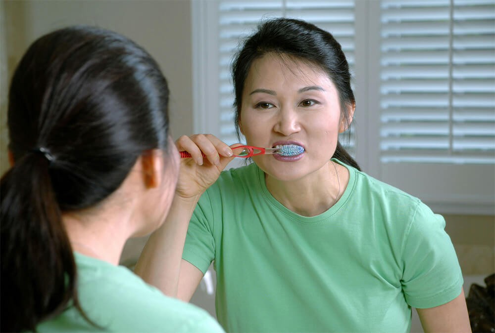 A woman brushing her teeth in front of a mirror.